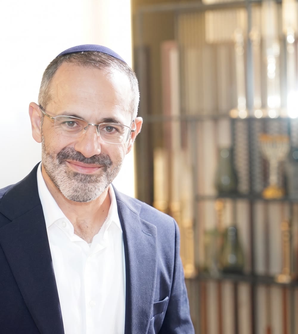 Portrait souriant de Fabrice, en blazer bleu marine, sur un fond flou chaleureux